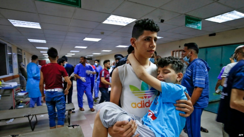 Seorang pemuda Palestina menggendong seorang anak laki-laki, terluka dalam serangan udara Israel, di dalam sebuah rumah sakit di Kota Gaza City pada, 12 Mei 2021. 